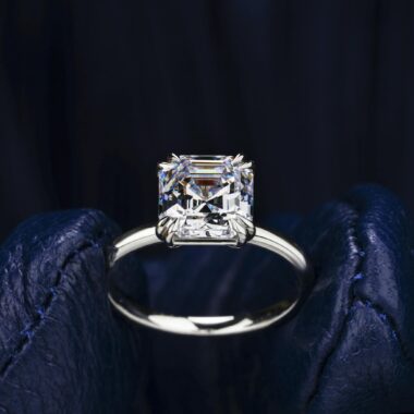 Close-up of a radiant diamond engagement ring held on blue leather, showcasing luxury and elegance.