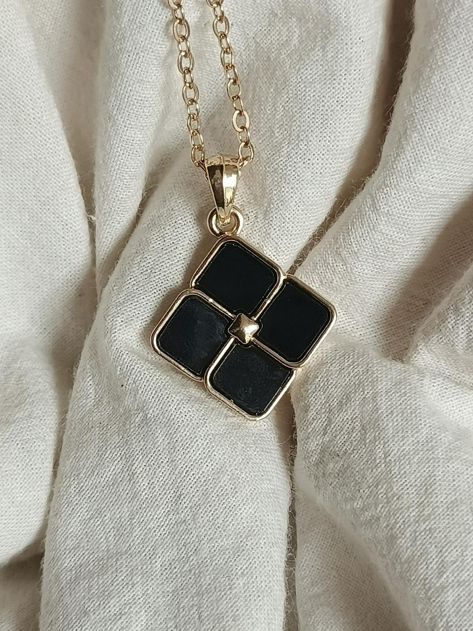 Close-up of a stylish black locket with gold chain on fabric background.