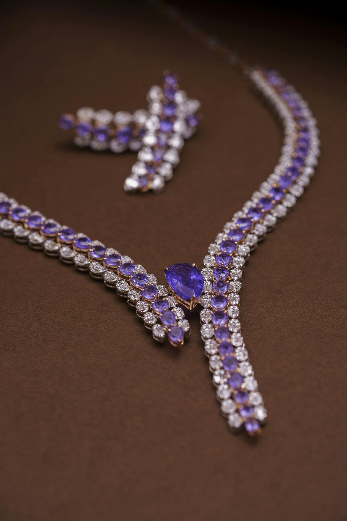 Luxury amethyst and diamond necklace and earring set on brown background.